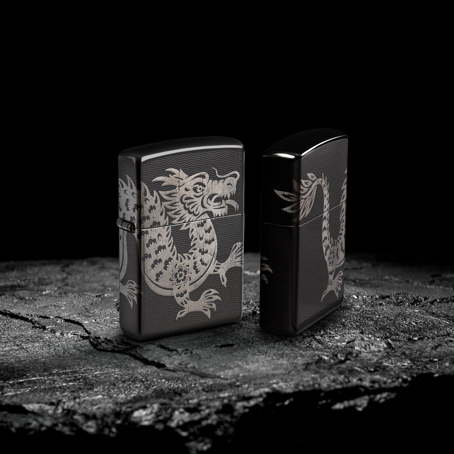 Lifestyle image of two Zippo Lucky Dragon Design High Polish Black Windproof Lighters standing on a rock surface with a black background.