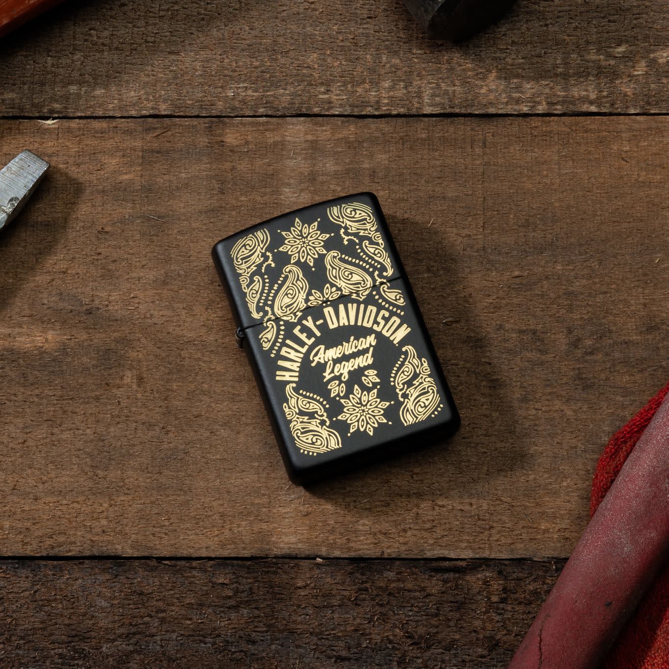 Lifestyle image of Zippo Harley-Davidson® American Legend Black Matte Windproof Lighter laying on a piece of wood with a screwdriver and pliers next to it.