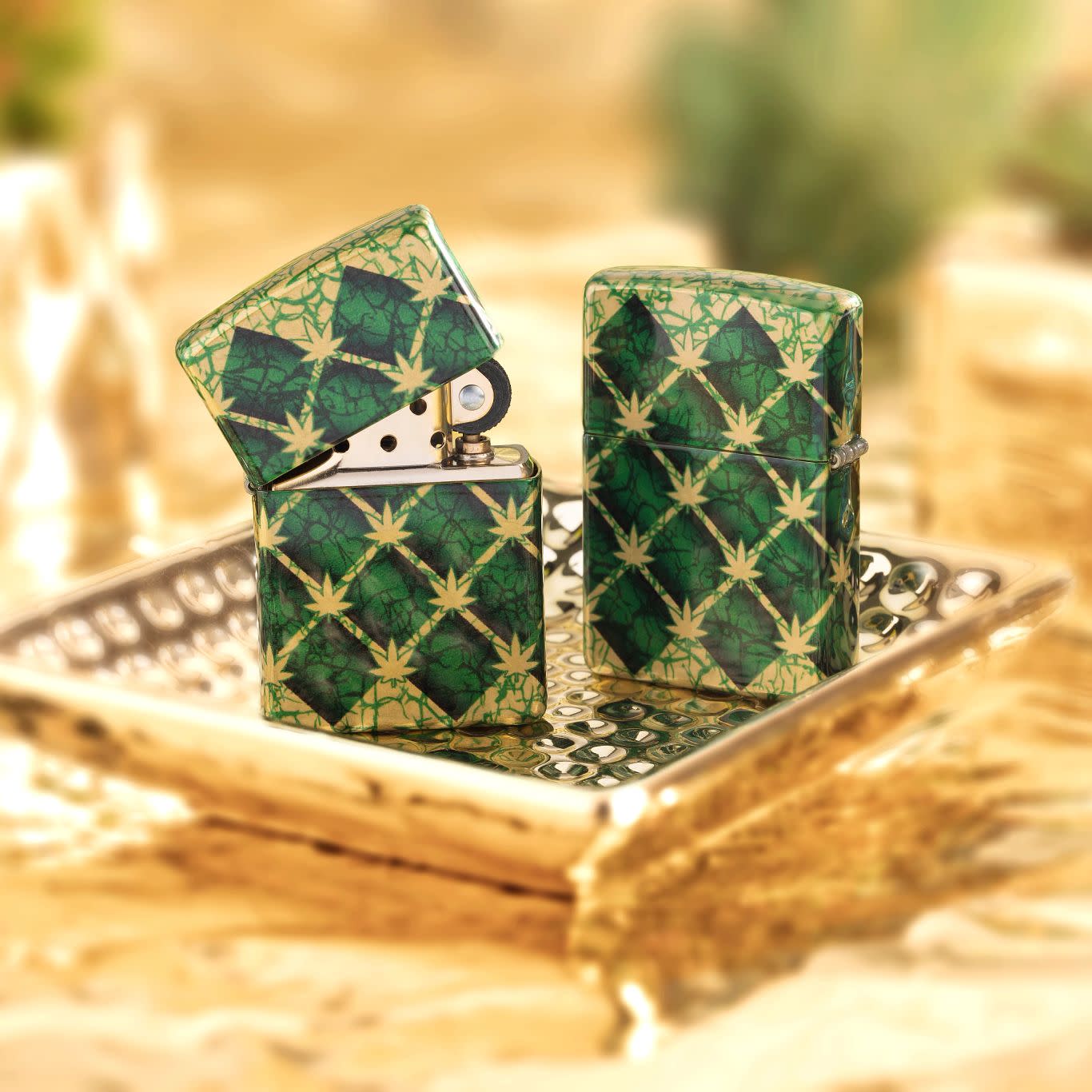 Lifestyle image of two Zippo Argyle Leaf Design 540 Tumbled Brass Windproof Lighters standing on a golden tray, one showing the front of the lighter and the other showing the back.