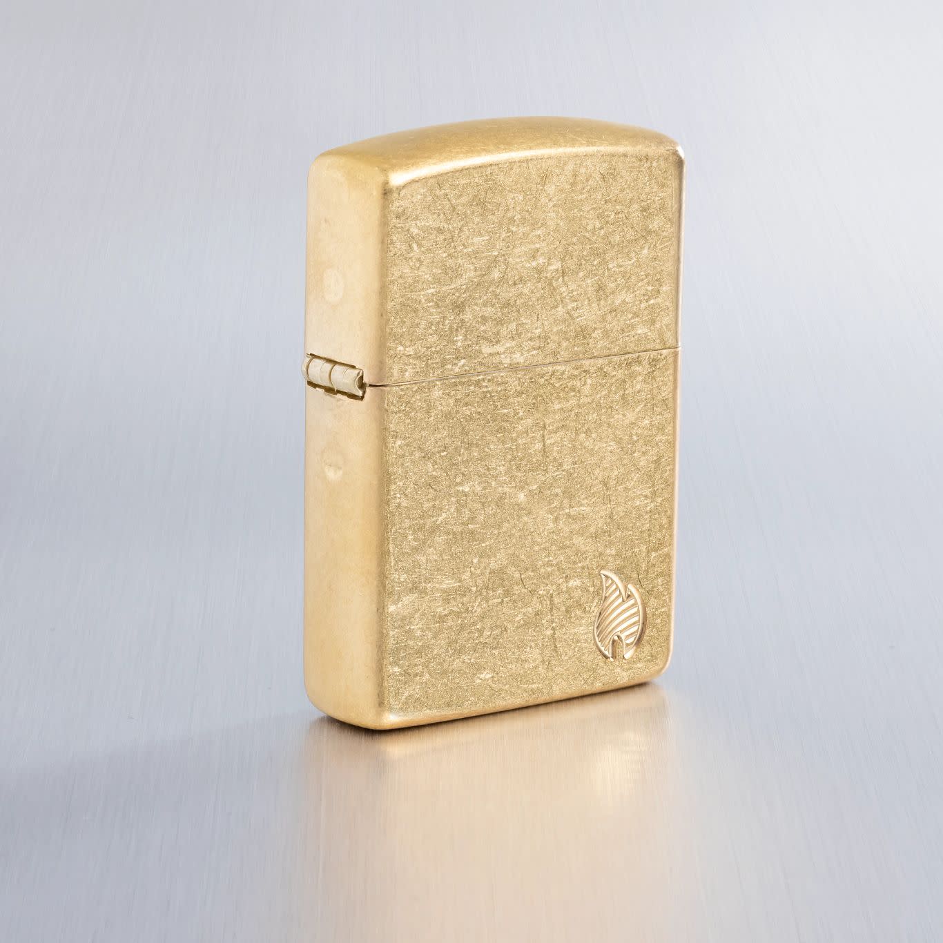 Lifestyle image of Zippo Armor® Series Flame Tumbled Brass Windproof Lighter on a light gray background.