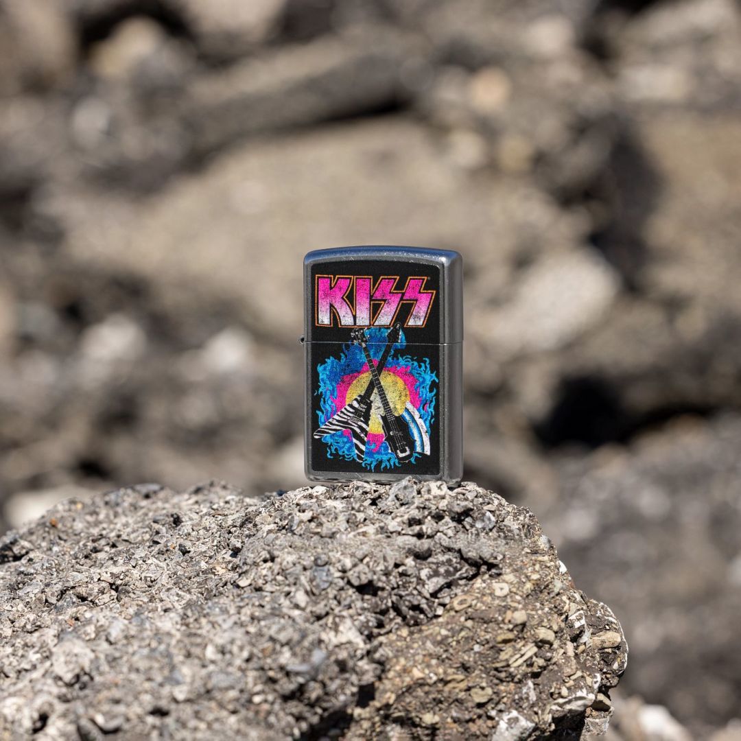 Lifestyle image of Zippo KISS® Axe Bass Design Street Chrome Windproof Lighter standing on a rocky surface showing the front and non-hinge side of the lighter with an out of focus rocky background. 

