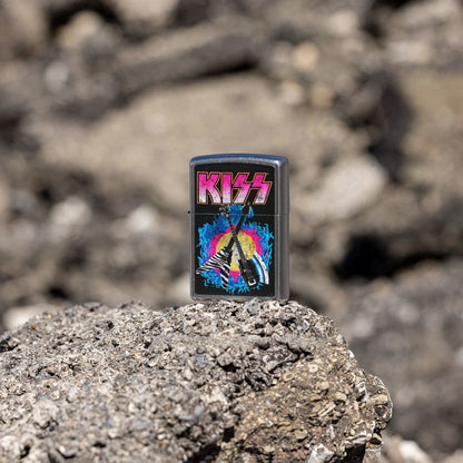 Lifestyle image of Zippo KISS® Axe Bass Design Street Chrome Windproof Lighter standing on a rocky surface showing the front and non-hinge side of the lighter with an out of focus rocky background. 

