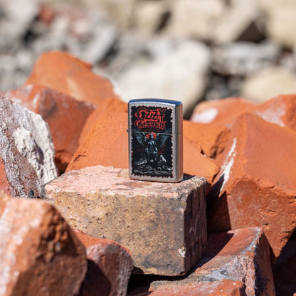 Lifestyle image of Zippo Ozzy Osbourne Angel Wings Design Street Chrome Windproof Lighter standing on a brick showing the front of the lighter with other bricks as the background. 

