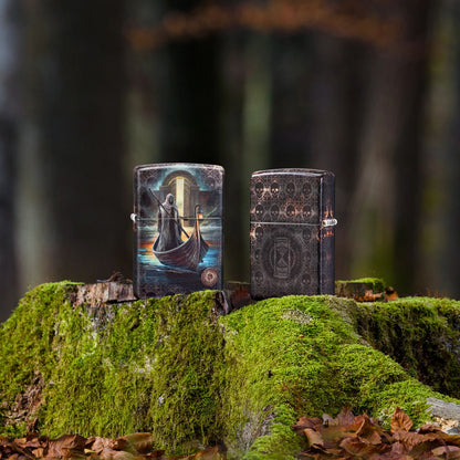 Lifestyle image of two Zippo Anne Stokes The Ferryman Design 540 Matte Windproof Lighters; one showing the front of the lighter and the other showing the back and hinge side of the lighter, both standing on a mossy tree stump. 

