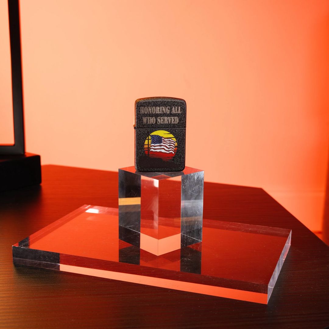 Lifestyle image of Zippo Honor Flag Design Black Crackle® Windproof Lighter standing on two clear blocks on a table showing the front of the lighter with a red light showing through the clear blocks and on to the wall.

