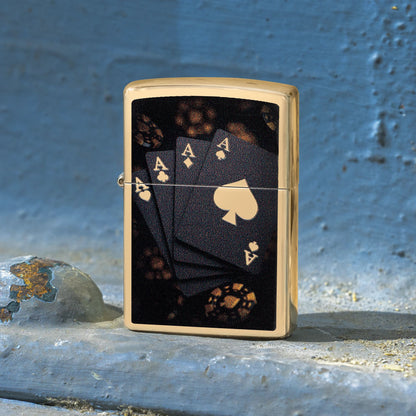 Lifestyle image of Zippo Lucky Aces Design High Polish Brass Windproof Lighter standing on a painted steel surface showing the front of the lighter. 

