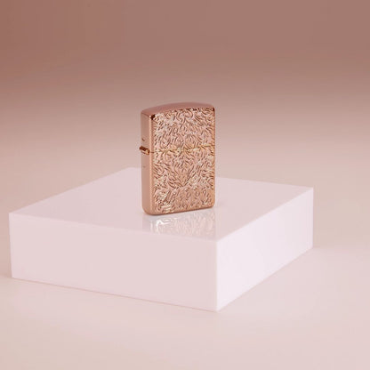 Lifestyle image of Zippo Carved Armor® Rose Gold Design Windproof Lighter standing on a riser in a pink background.