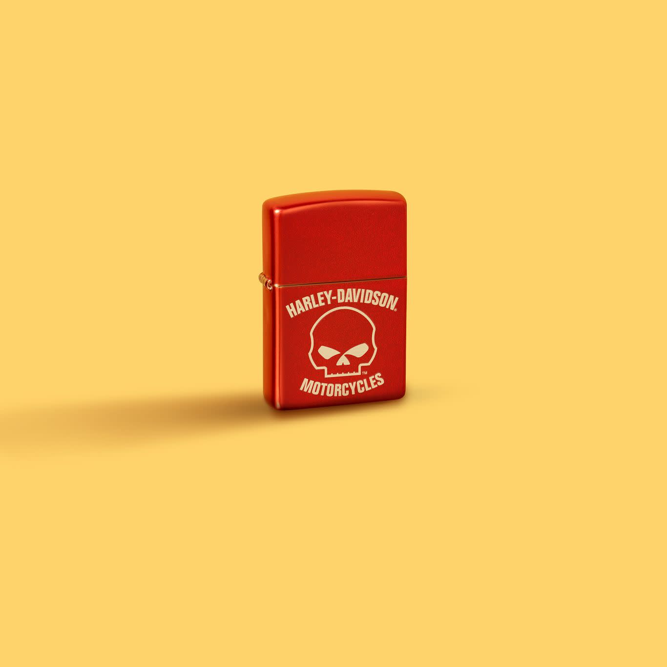 Glamour shot of Zippo Harley-Davidson Laser Skull Metallic Red Windproof Lighter standing in a yellow scene.