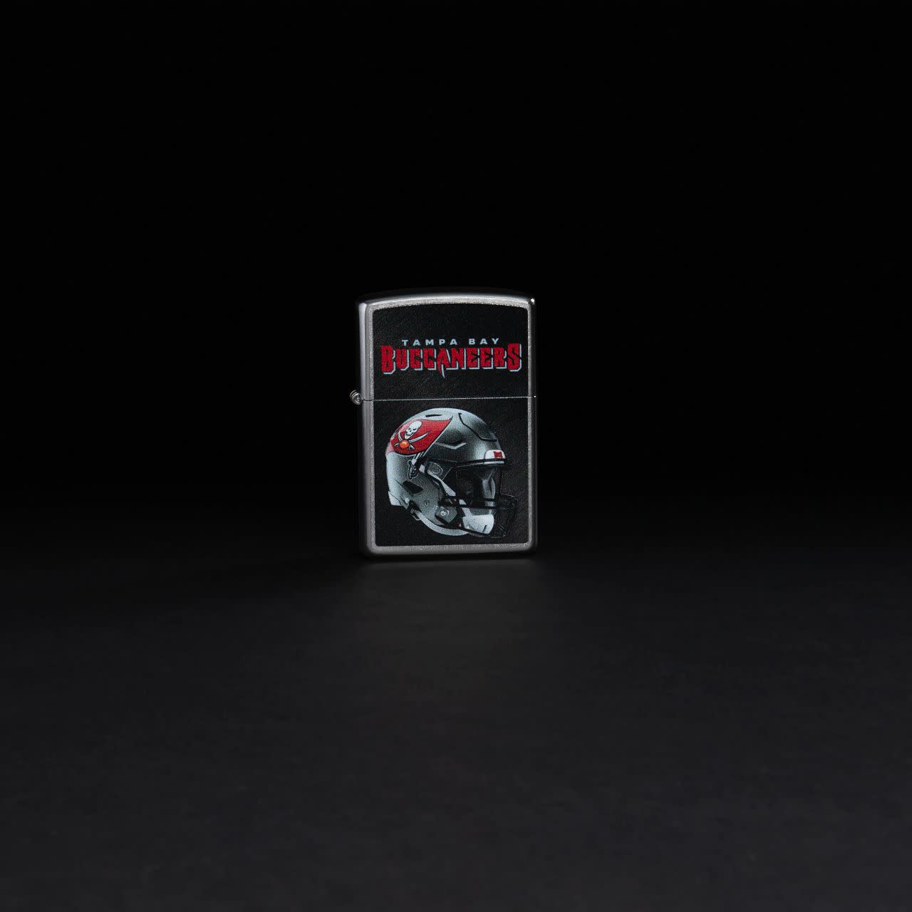 Lifestyle image of NFL Tampa Bay Buccaneers Helmet Street Chrome Windproof Lighter standing in a black background.