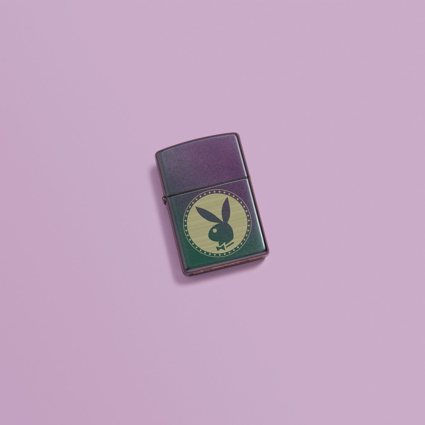 Lifestyle image of Playboy Engraved Rabbit Head Iridescent Windproof Lighter laying on a pink background.