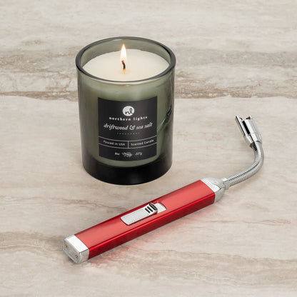 Lifestyle image of Candy Apple Red Rechargeable Candle Lighter & 8 oz Driftwood & Sea Salt Candle lit on a countertop.