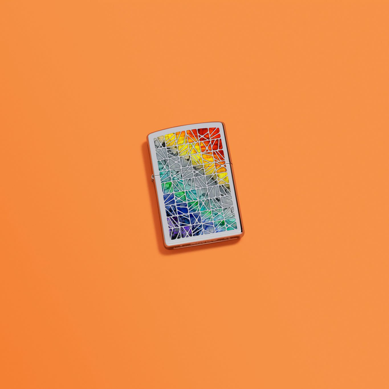 Lifestyle image of Fusion Pattern Design High Polish Chrome Windproof Lighter laying on an orange background.