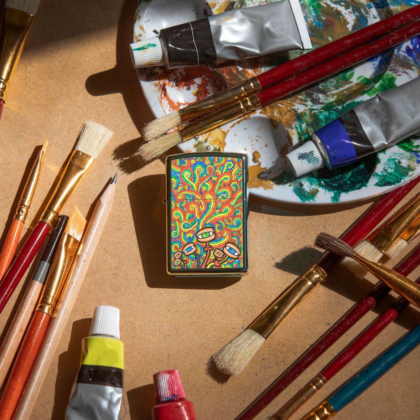 Lifestyle image of Psychedelic Imagery Design High Polish Teal Windproof Lighter laying with painting equipment.