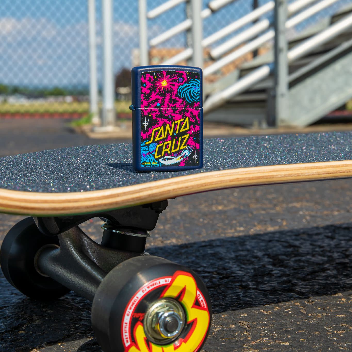 Lifestyle image of Santa Cruz Outer Space Galaxy Design Navy Matte Windproof Lighter standing on a skateboard.