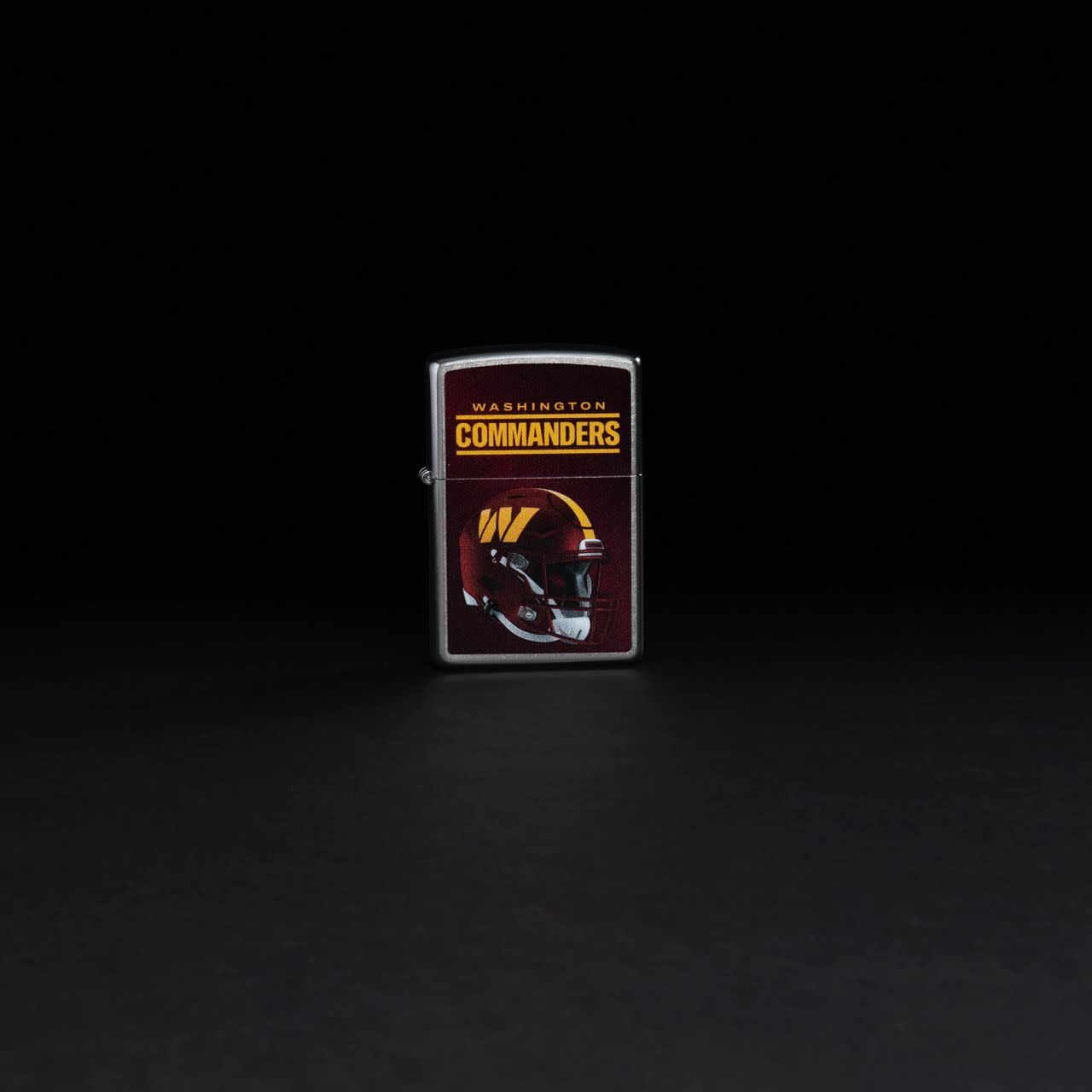 Lifestyle image of NFL Washington Commanders Helmet Street Chrome Windproof Lighter standing in a black background.