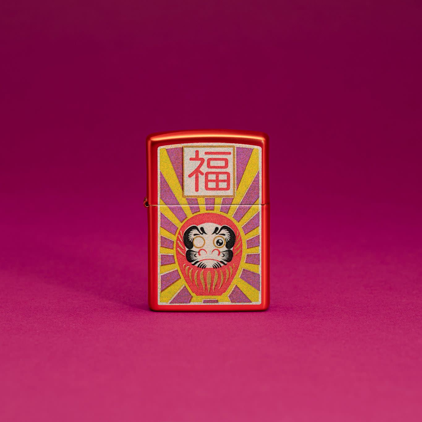 Lifestyle image of Zippo Daruma Design Metallic Red Windproof Lighter standing in a red scene.