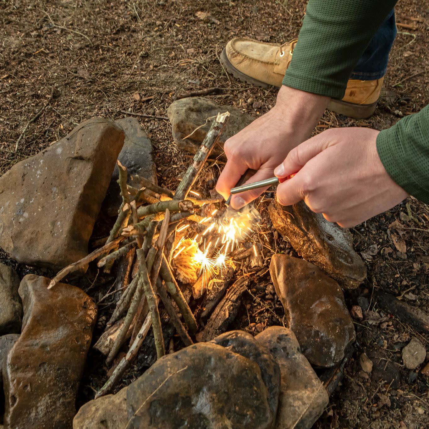 Lifestyle image of man striking the Mag Strike to create a spark over the tinder shreds to start a fire.