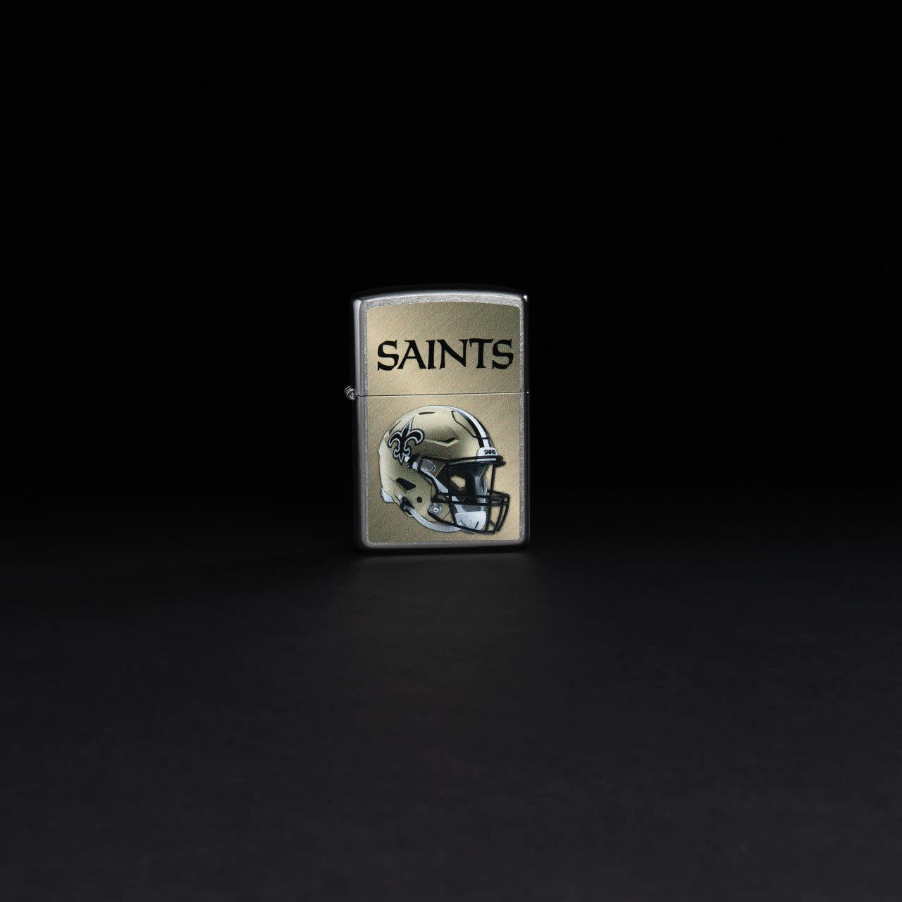 Lifestyle image of NFL New Orleans Saints Helmet Street Chrome Windproof Lighter standing in a black background.